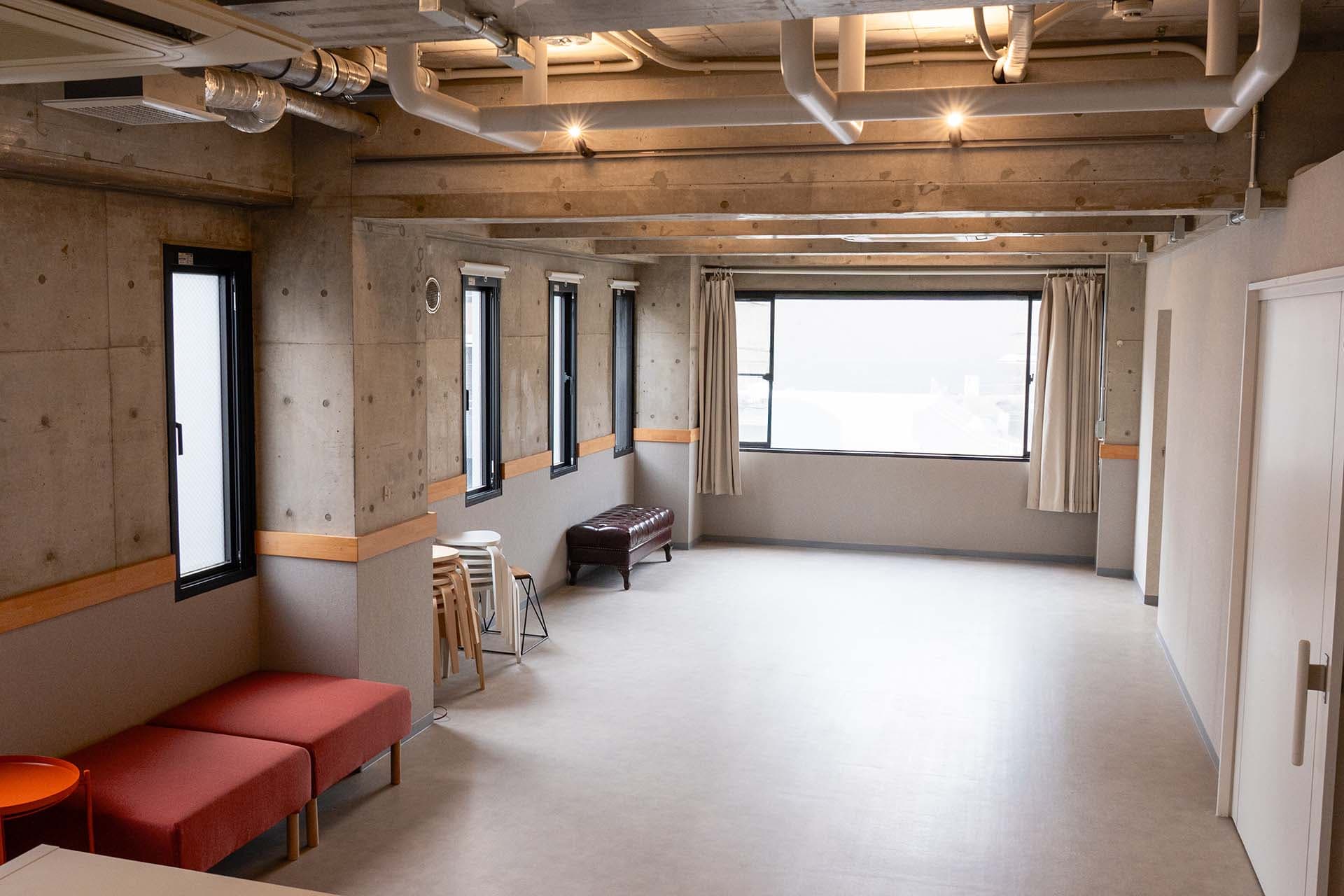 41㎡の広々としたメインフロア。コンクリートの質感と木製家具が調和した空間。赤いソファがあり、待機スペースとしても活用できます。