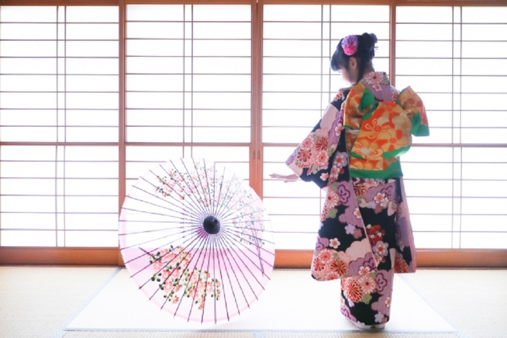 和室の障子の前で和傘をもつ七五三の女の子